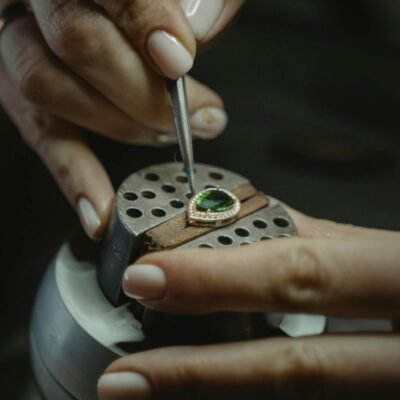 A skilled jeweler carefully crafting an emerald ring using a tweezer, showcasing craftsmanship.