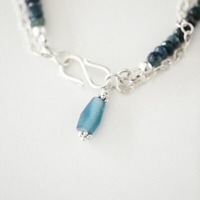 Close-up image of an elegant silver bracelet featuring blue gemstones on a white background.