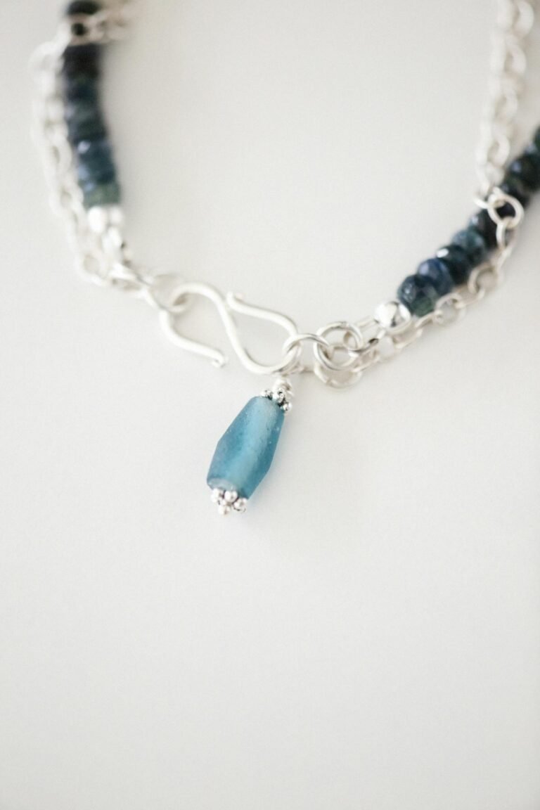Close-up image of an elegant silver bracelet featuring blue gemstones on a white background.