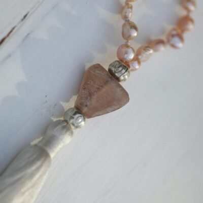 Close-up of a pearl necklace with gemstone pendant on a wooden surface.